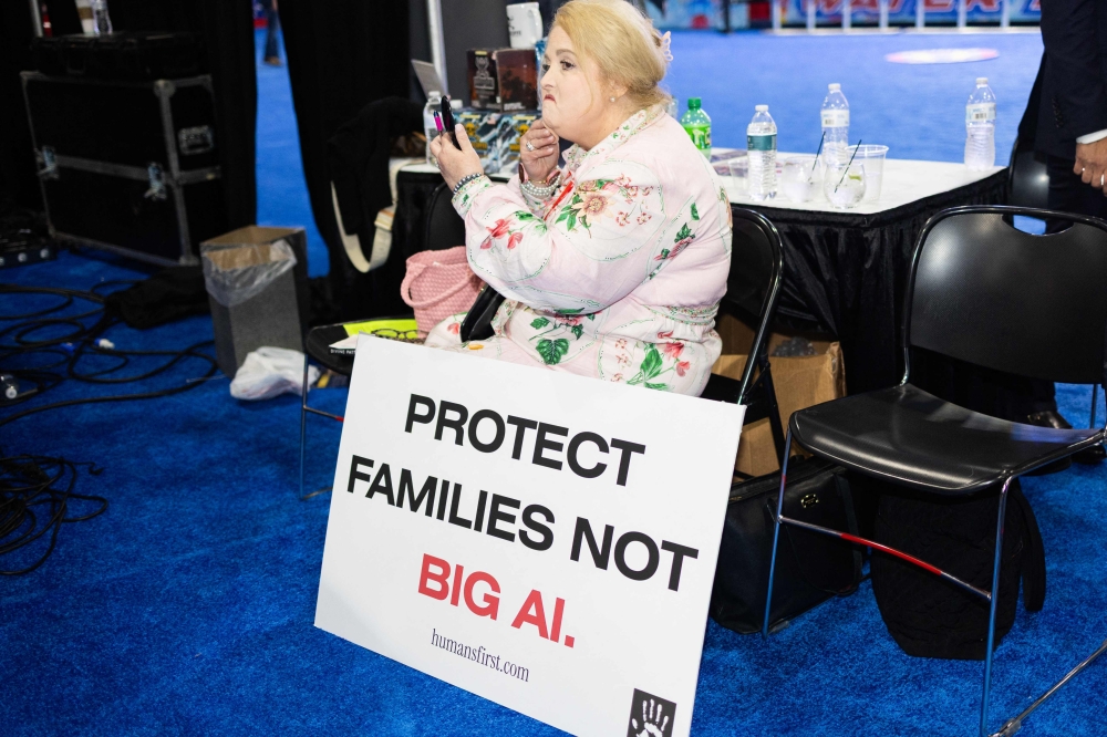 A woman adjusts her makeup while sitting with a sign expressing concerns about artificial intelligence at the Conservative Political Action Conference in Grapevine, Texas, on March 26, 2026. — AFP pic