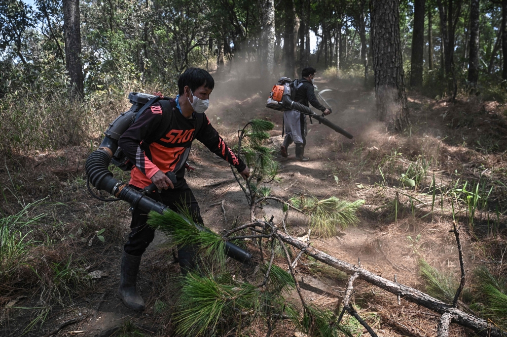 Volunteer firefighters from Hmong Doi Pui village using leaf blowers to clear a firebreak in the Doi Suthep-Pui National Park area of Chiang Mai on March 26, 2026 during the dry season while others scan for smoke on live feeds from their phones. — AFP pic
