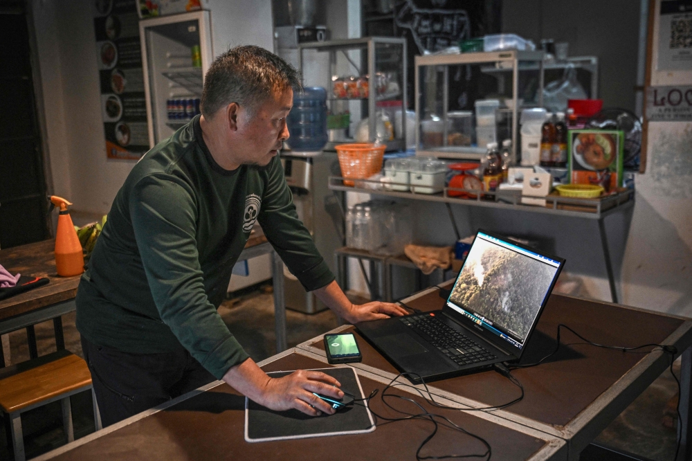 Hmong volunteer firefighter Mongkol Yingyotmongkolsaen looks through old footage of forest fires at his home in the Hmong Doi Pui Village in the Doi Suthep-Pui National Park area of Chiang Mai, employing new tech to combat wildfires. — AFP pic