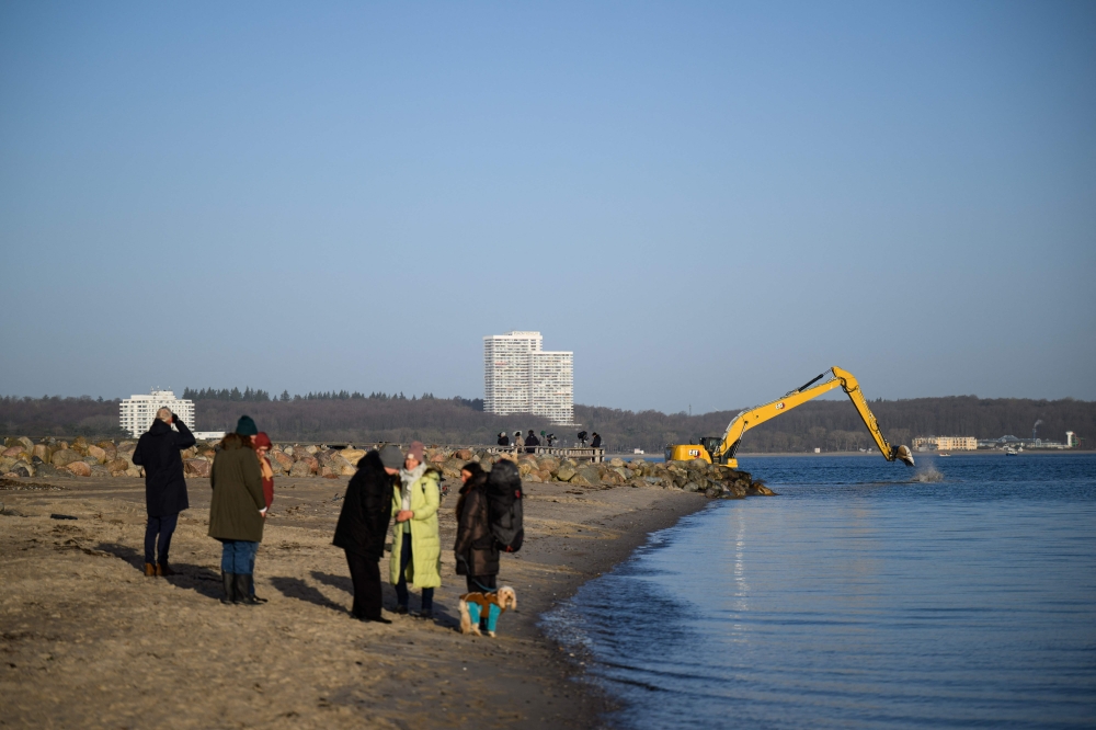 Onlookers stand on the beach in Niendorf, northern Germany, on March 27, 2026, with heavy machinery still visible in the background after a humpback whale that had run aground off the Baltic Sea coast apparently freed itself overnight following a large-scale rescue operation. — AFP pic 