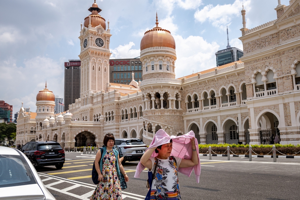 A woman uses her clothing to shield herself from the sun during hot weather in Kuala Lumpur. — Picture by Firdaus Latif.