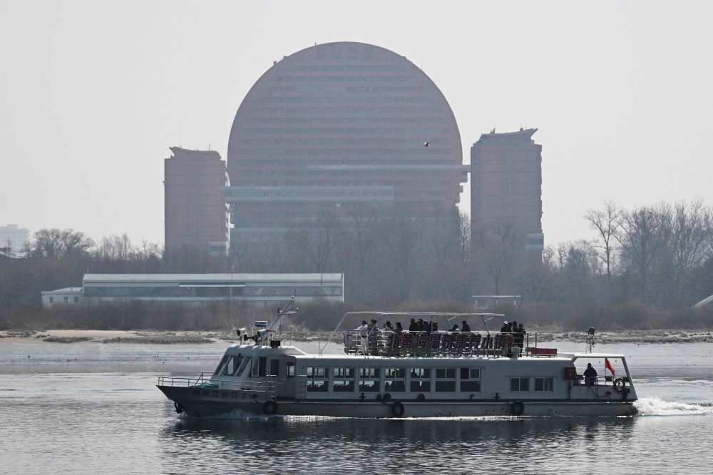 A Chinese tour boat cruises on the Yalu River past a hotel in the North Korean town of Sinuiju, opposite the border city of Dandong, in China's northeast Liaoning province on March 26, 2026. — AFP pic