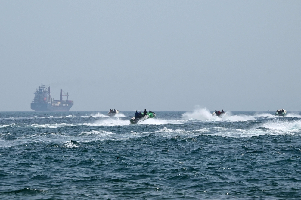 Small boats loaded with merchandise sail past the St Kitt's and Nevis-flagged container ship Marsa Victory in the waters of the Strait of Hormuz off the coast of Khasab in Oman痴 northern Musandam peninsula on June 25, 2025. Seafarers’ helplines say they are overwhelmed with messages from crews stuck in the Gulf by the Middle East war, desperately seeking repatriation, compensation and onboard supplies. — AFP pic 