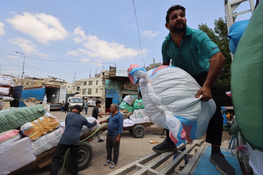 Workers load goods onto trucks at a transport garage in Baghdad on March 30, 2026, as disruptions in the Strait of Hormuz constrain access to Iraq’s Umm Qasr port, pushing trade onto costlier overland routes. — AFP pic