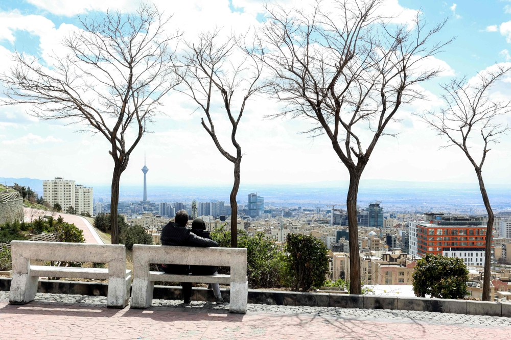 A couple sits on a bench at a park in northern Tehran overlooking the Iranian capital's skyline with Milad (Birth) Tower, the tallest tower in the country at 435 metres, pictured in the background, on March 30, 2026. — AFP pic