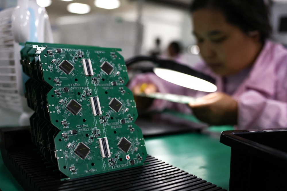 An employee inspects a printed circuit board at a factory, which is in partnership with Agilian Technology, in Dongguan. — Reuters pic
