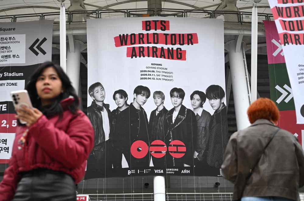 Fans walk in front of a large banner featuring K-pop boy band BTS at a stadium in Goyang on April 9, 2026. — AFP pic