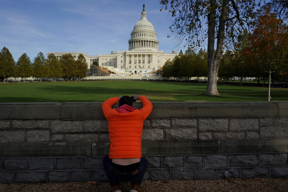 A person squats while using a mobile phone, with the US Capitol building on the background, on the day Republican US Senator John Thune (R-SD) was elected to become the next Senate Majority Leader, following the US Senate Republicans leadership election, on Capitol Hill in Washington November 13, 2024. — Reuters pic  