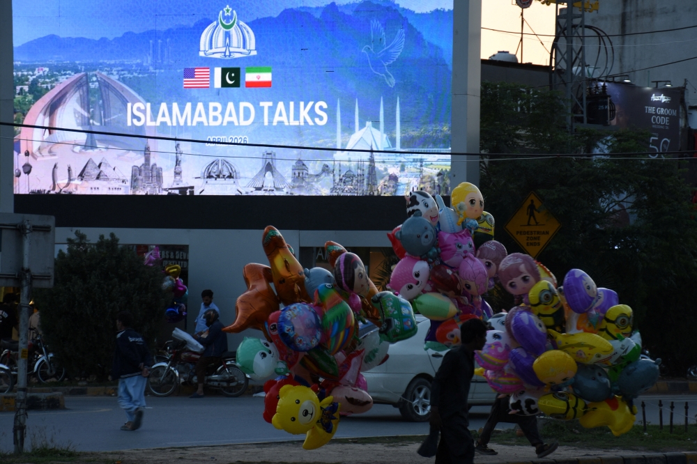 A balloon seller walks near a screen with an image referring to the US-Iran peace talks on the day they are held in Islamabad April 11, 2026. — Reuters pic 