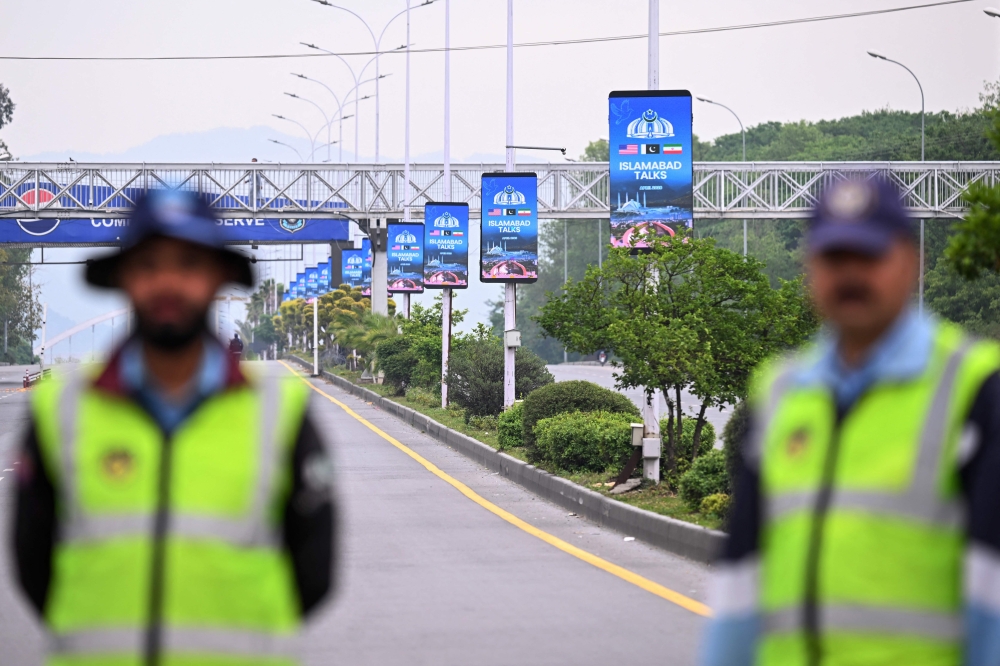 Policemen stand guard at a checkpoint near the pole banners referencing the US-Iran peace talks in Islamabad on April 11, 2026. — AFP pic 