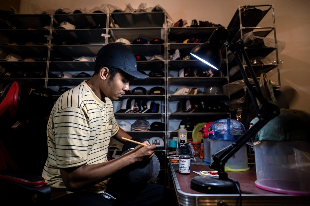 Ahmad Fadhil Nazeri, 29, repaints a worn cap during an interview in Wangsa Maju, Kuala Lumpur, recently, where he spoke about giving faded headwear a new lease of life through his hat restoration business. — Bernama pic