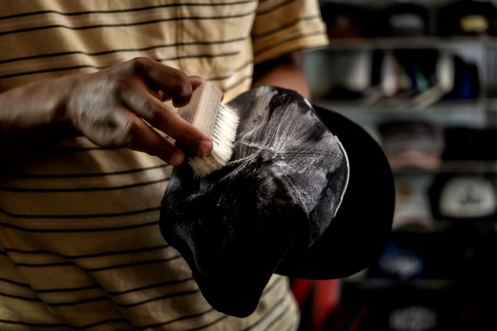 Ahmad Fadhil Nazeri, 29, cleans a cap at his shop in Wangsa Maju, Kuala Lumpur, recently. — Bernama pic