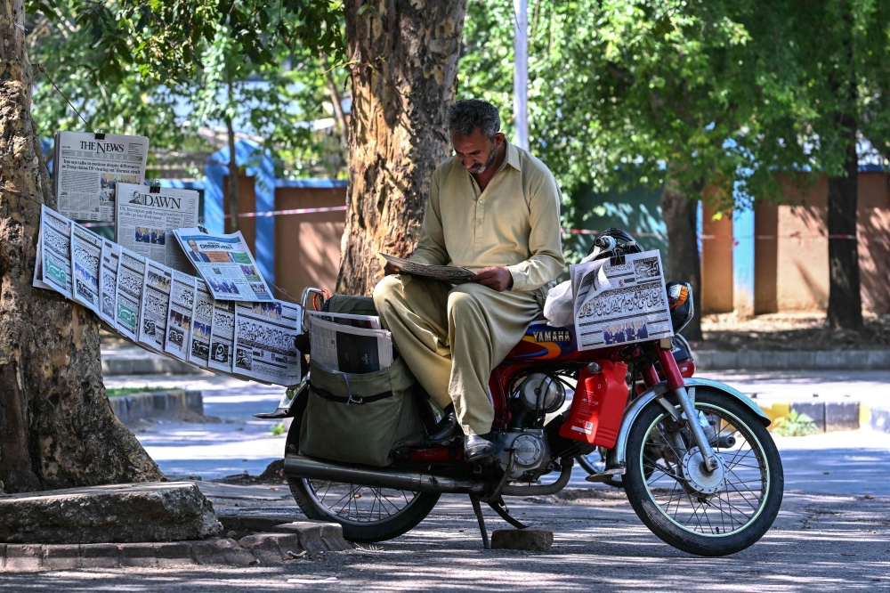A vendor reads a newspaper displayed on a roadside after the US-Iran peace talks in Islamabad on April 12, 2026. — AFP pic