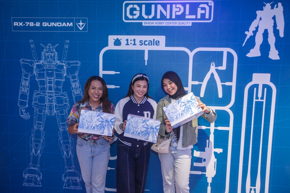 Fans pose with their newly purchased Gunpla model kits in front of a themed photo wall during the opening of the first Gundam Base brand store at Fahrenheit88 in Malaysia. April 14, 2026—Picture by Raymond Manuel