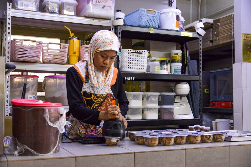 Nurul Asyiqin seals cookies using an aluminium sealing device to ensure the capsules are airtight and give the container a modern aesthetic style. — Bernama pic