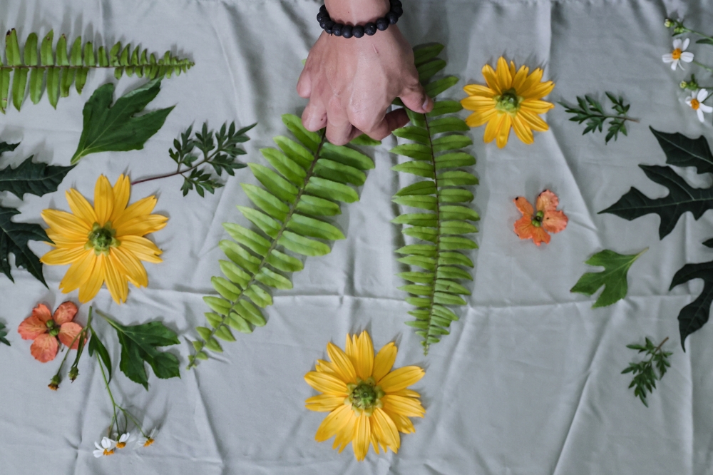 Misbaahussalam Zakaria arranges leaves and flowers to create patterns for eco‑print products at his home in Benut. — Bernama pic