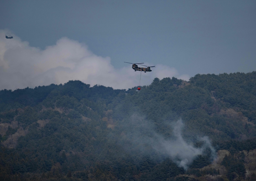 Two helicopters doing water drops fly over smoke from a forest fire on the side of a hill side near the town of Otsuchi, in Iwate Prefecture on April 25, 2026. — AFP pic 