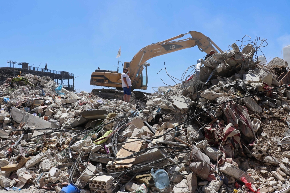 Resident Mohamad Ali Hijazi (centre) stands next to an excavator clearing the rubble of destroyed buildings at a residential area in Tyre on April 23, 2026. Clutching a battered photo album, Hijazi searched a mountain of rubble in south Lebanon's Tyre for mementoes of his family, killed in an Israeli strike minutes before a ceasefire took hold. — AFP pic 