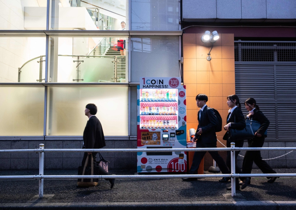 People walking to a metro station pass a vending machine on a side street at the end of the day in Tokyo’s Shinjuku April 13, 2026. — AFP pic