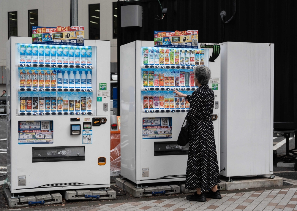 A woman gets a drink from a vending machine at a major intersection in Tokyo’s Ginza district on April 13, 2026. — AFP pic