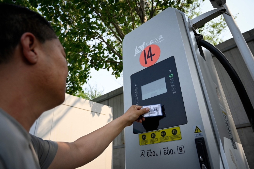 A driver swiping a card to charge his electric truck at a charging station in Beijing. — AFP pic  