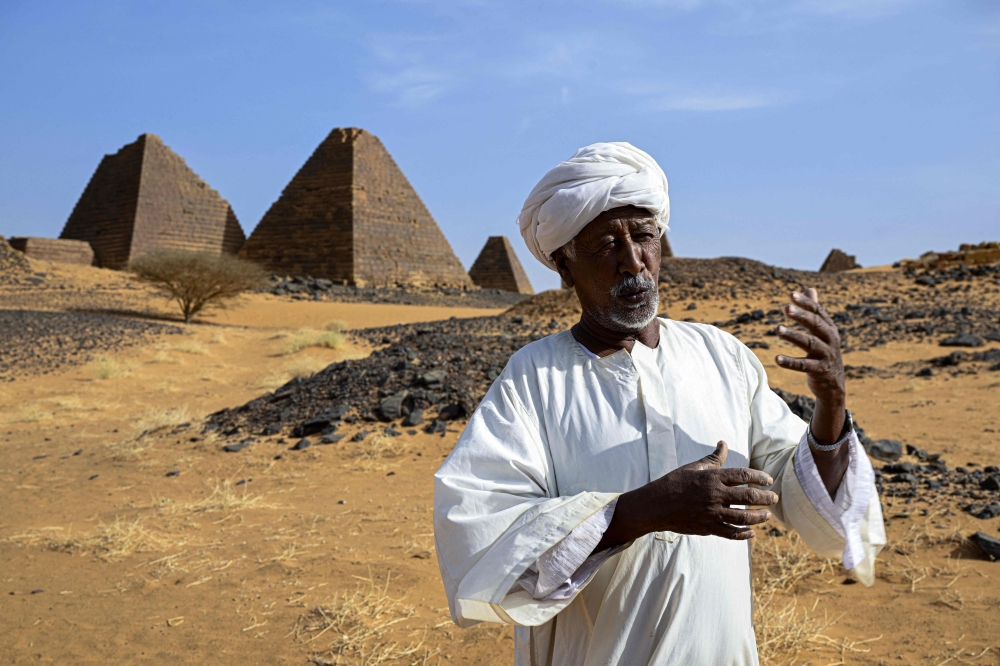 Local site guard Mostafa Ahmed speaks in front of pyramids standing in the Meroe desert, at one of the archaeological sites of the so-called Island of Meroe on the eastern shore of the Nile River. — AFP pic 