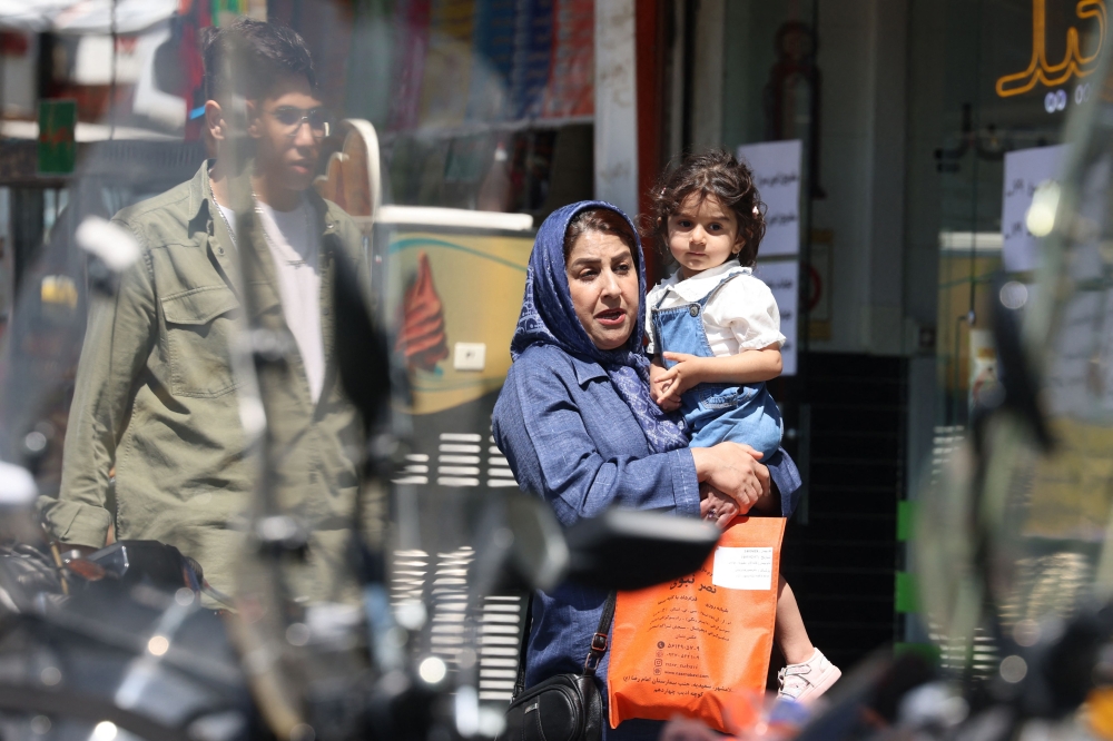 An Iranian woman carrying a child walks at the Revolution Square in Tehran on April 28, 2026. — AFP pic  