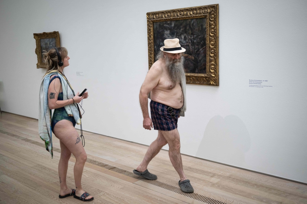 Visitors wearing a swimsuit walk past the painting “Rochers a Fontainebleau” (“Rocks at Fontainebleau”, 1893) by French painter Paul Cezanne during the experience called “bathers’ day” (“journée des baigneurs et des baigneuses”) inspired by Italian artist Maurizio Cattelan, on the occasion of the exhibition “Cezanne” at the Beyeler Foundation in Riehen, northern Switzerland on May 1, 2026. — AFP pic