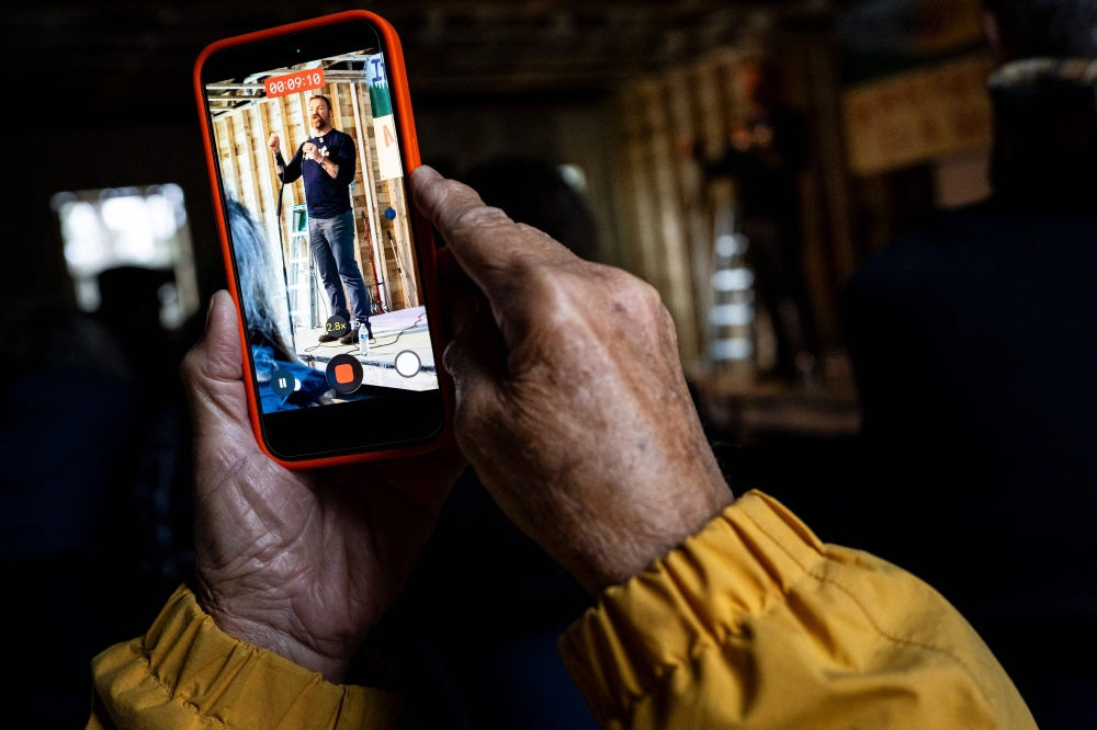 An attendee records US Senate candidate from Maine, Graham Platner, during a campaign townhall event on May 2, 2026 in Appleton, Maine. — Getty Images via AFP