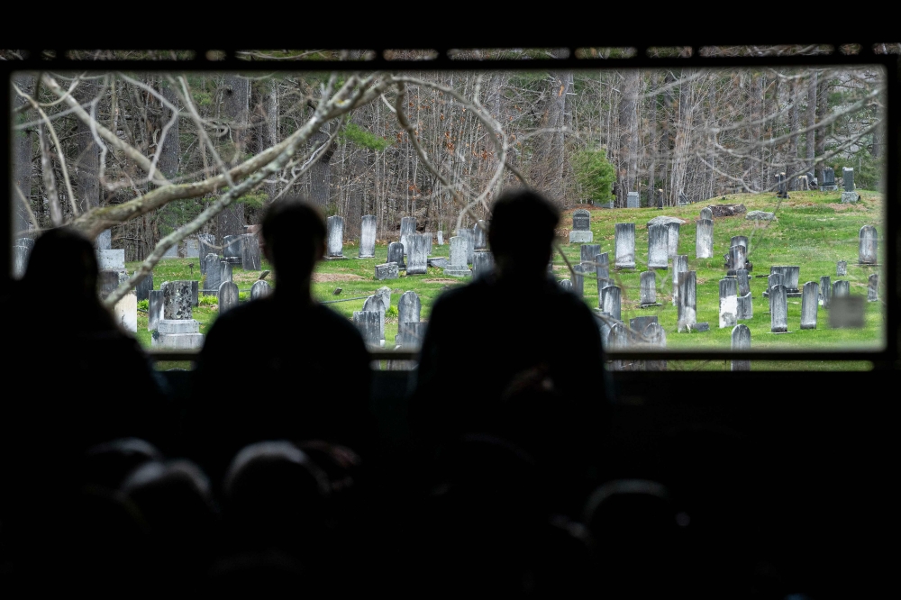 A graveyard is seen through a window behind attendees during a Graham Platner for Senate campaign townhall event on May 2, 2026 in Appleton, Maine. — Getty Images via AFP