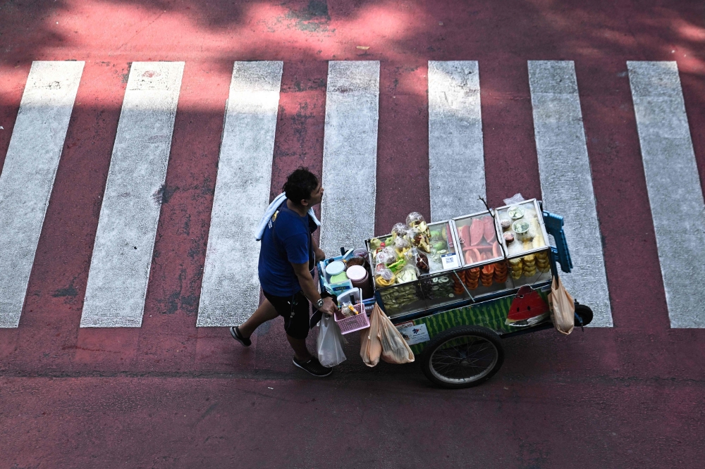 A street vendor pushing a cart of fresh fruit in Bangkok, Thailand across the road.  — AFP pic 