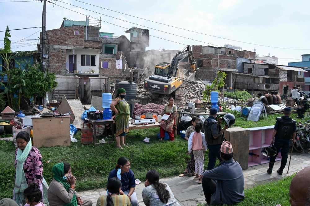 People watch as heavy construction equipment is used to demolish squatter settlements near the Bagmati River in Kathmandu on May 1, 2026. — AFP pic