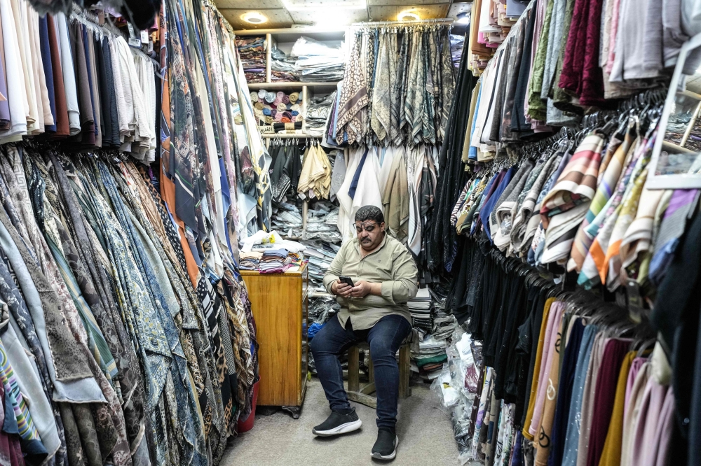 A shopkeeper of a clothing store passes time by scrolling through his phone as he sits and waits for customers in the Old City of Najaf. — AFP pic  