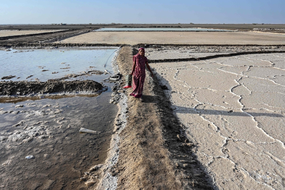 This photograph taken on April 29, 2026 shows a salt pan worker carrying rubber boots as she walks across an alkali flat at the Little Rann of Kutch region in Gujarat. India faces challenging heatwaves each year, but few places endure conditions as searing as the country's western desert salt pans, where workers rely on simple techniques to survive almost unbearable temperatures. In Gujarat's Little Rann of Kutch summer temperatures routinely cross 45 degrees Celsius, and can climb to 47–48C. Up to 50,000 workers spend eight months on the remote salt pans without electricity or healthcare, relying on a tanker to deliver drinking and washing water every 25 days. — AFP pic