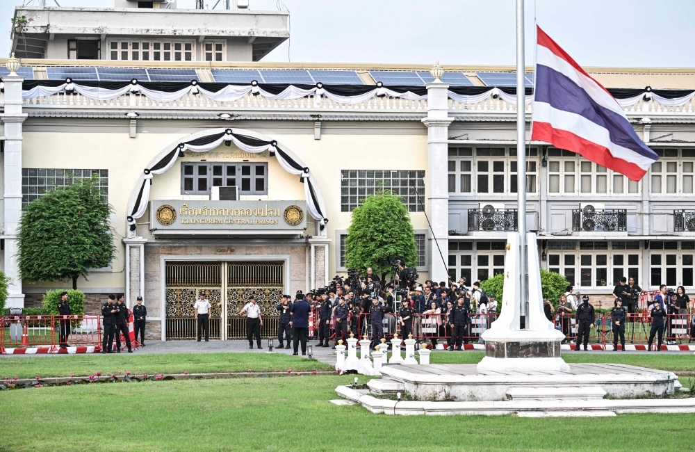 Security stand guard and members of the media wait ahead of the expected release of Thailand's former prime minister Thaksin Shinawatra at the entrance of Klong Prem Central Prison in Bangkok on May 11, 2026. — AFP pic