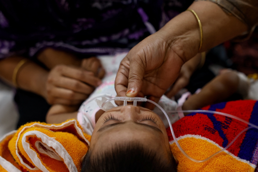 A woman adjusts a tube to ensure extra oxygen supply to a child infected with measles receiving treatment at the DNCC Hospital, following an outbreak across the country, in Dhaka May 6, 2026. — Reuters pic