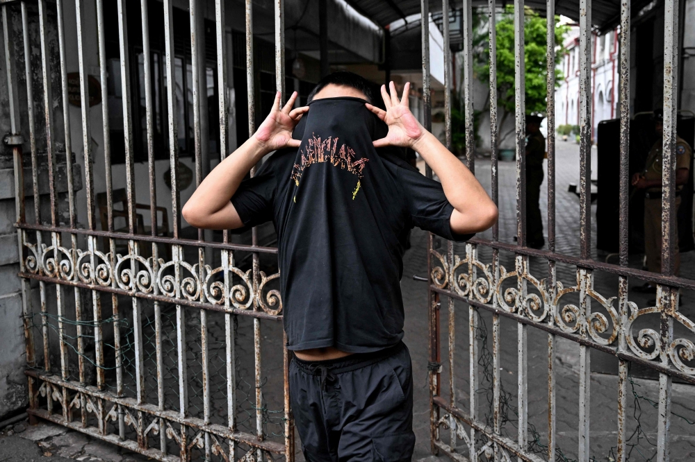 A detained Chinese national suspected of running cyberscam centres is escorted to a prison after his arrest in Colombo May 9, 2026. — AFP pic