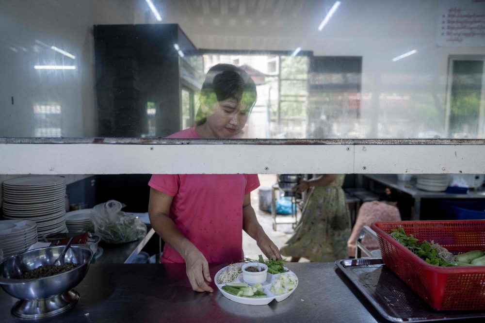 Una vendedora prepara comida mientras espera a los clientes en un restaurante de comida tradicional de Rakhine en Yangon el 13 de mayo de 2026. - Foto de AFP