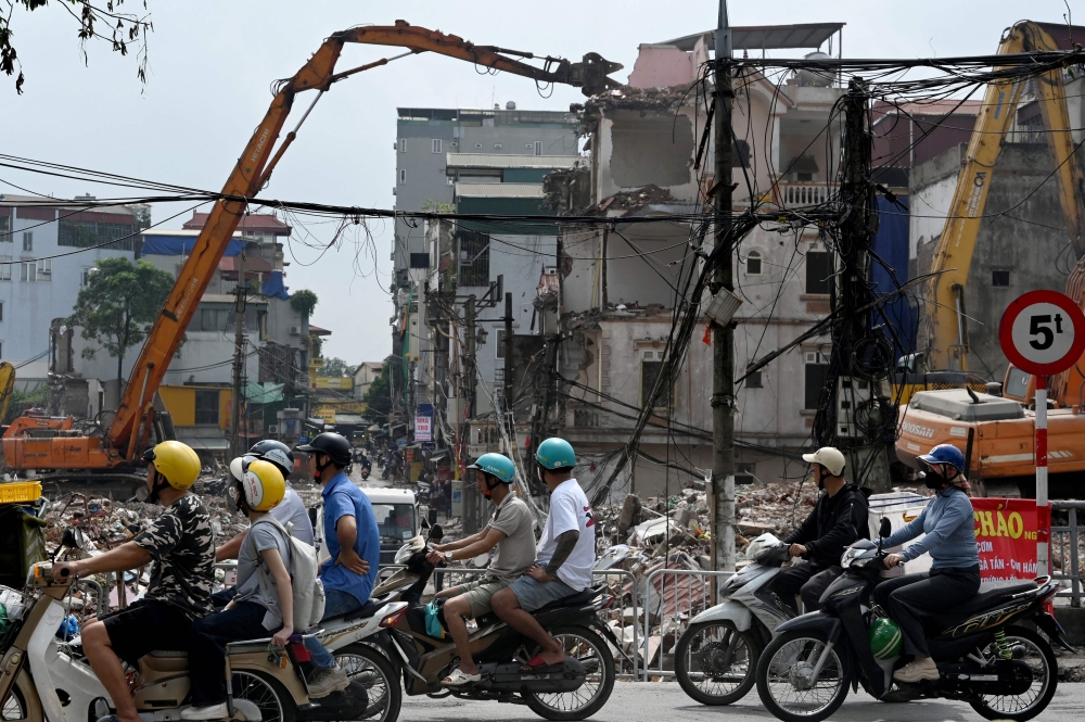 People ride motorcycles past a demolition site of former residential buildings to make way for an expanded road network in Hanoi May 18, 2026. — AFP pic
