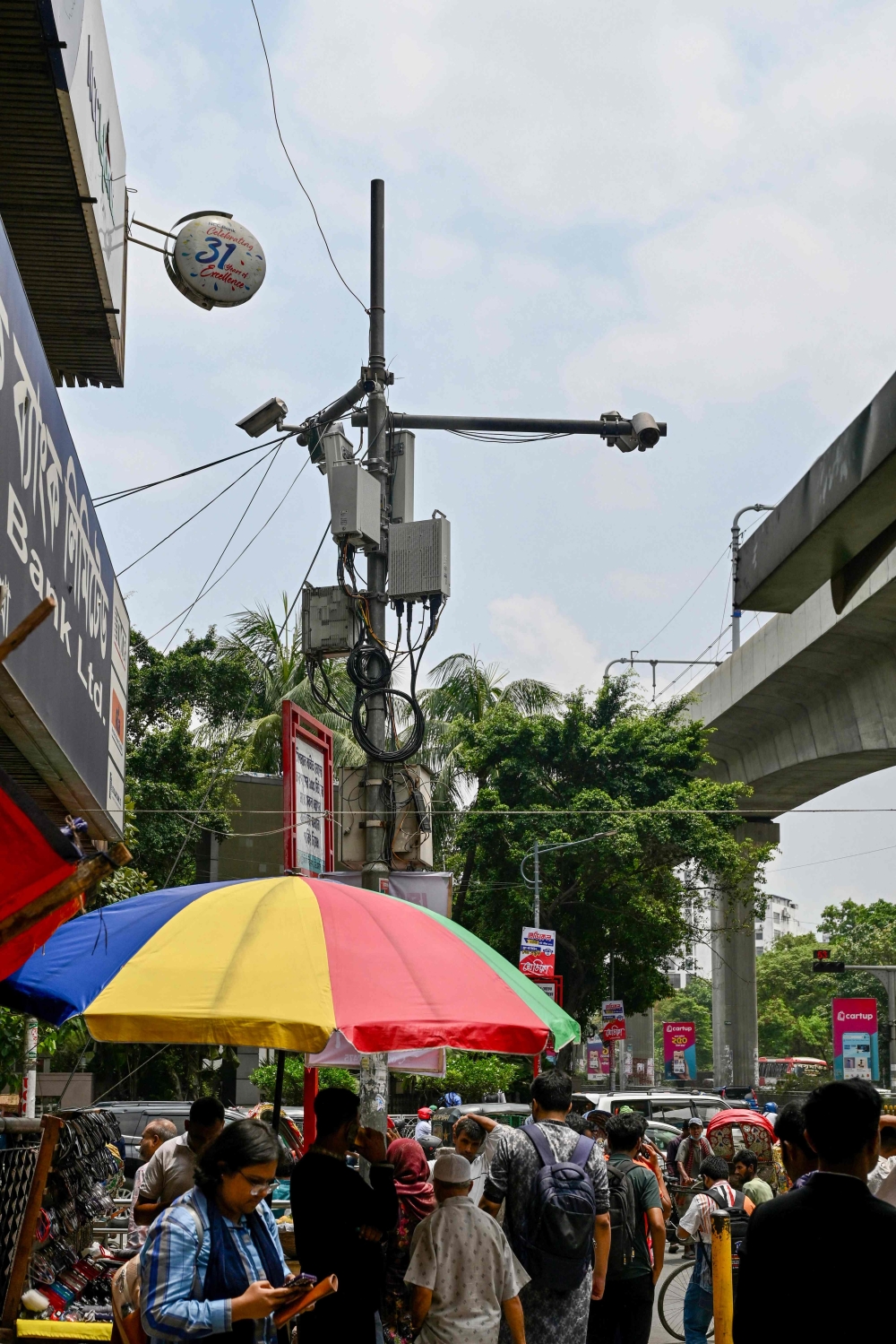 People travel past an AI-based traffic management system (C) installed along a road in Dhaka May 14, 2026. — AFP pic