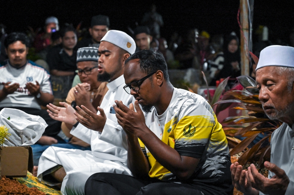 Azizul Abdul Aziz, 48, says a prayer after the burial of his daughter, Nur Izzati Humaira Azizul, 18, at the Felda Trolak Utara Muslim cemetery after she died while hiking Bukit Changkat Asa. — Bernama Photo