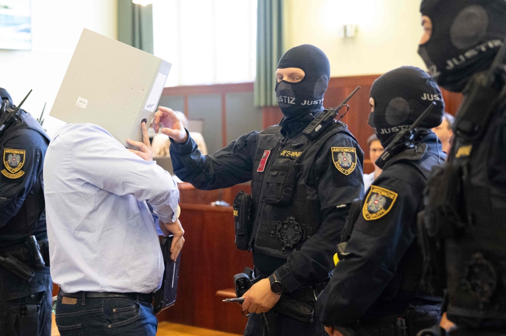 A defendant in handcuffs hides his face behind a folder as he is escorted to the courtroom by justice officers as the verdict in a trial over a plot to attack a Taylor Swift concert in Vienna is awaited at a court in Wiener Neustadt, Austria, on May 28, 2026. — AFP pic