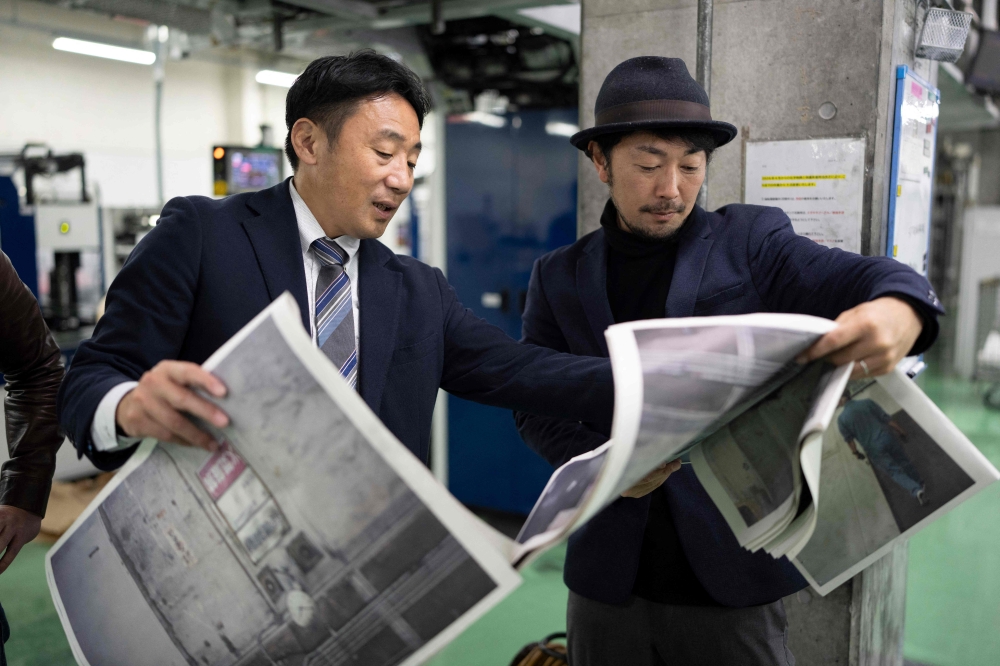 This picture taken on March 19, 2026 shows photographer Kazuma Obara (R) and a staff member inspecting the printing quality of his work titled “The Newspaper” at the Kyoto Shimbun factory in Kumiyama, Kyoto prefecture. Despite the decline of the publishing industry, self-publication and handmade 
