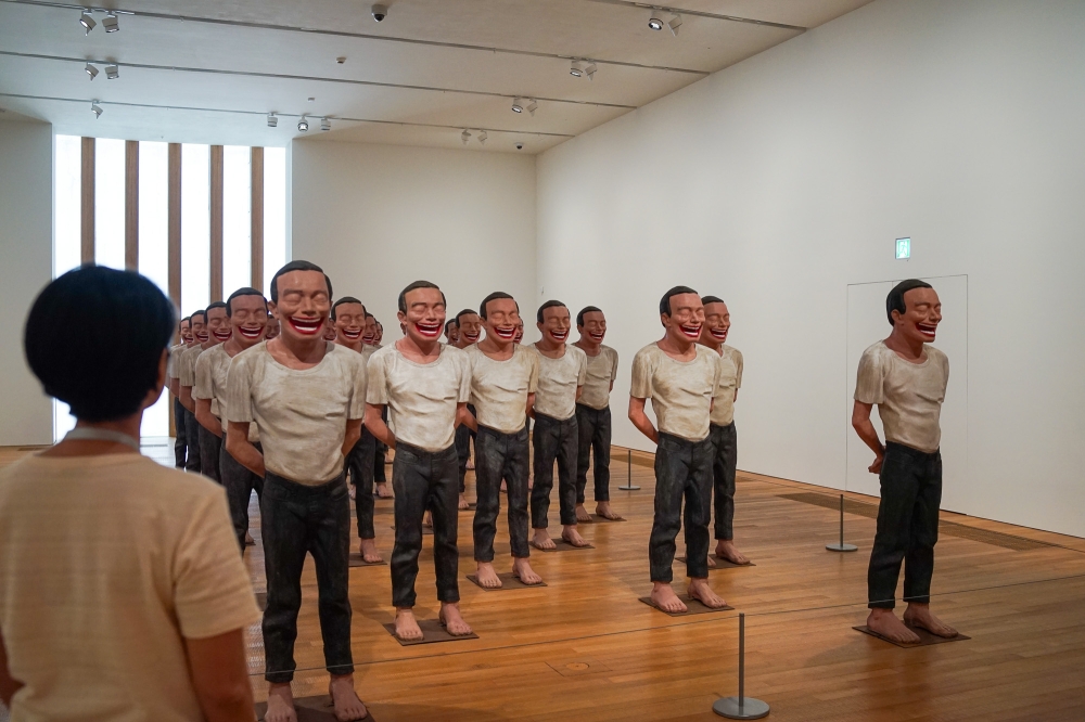A visitor of the 'M  Sigg Collection: Inner Worlds' exhibition is seen here looking at artist Yue Minjun’s artwork called '2000 A.D.', where 25 life-sized sculptures are arranged like the famous terracotta warriors in Emperor Qin Shihuang’s mausoleum. — Picture by Ida Lim