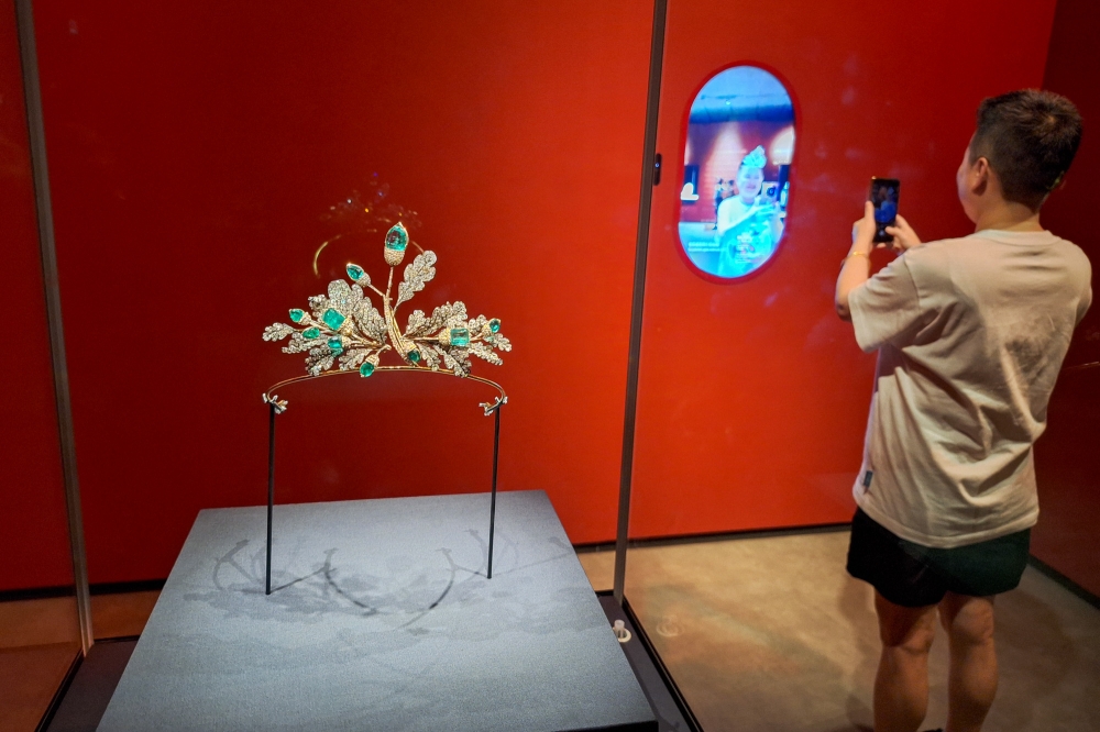 A Hong Kong Palace Museum visitor is seen here snapping a photograph of the augmented-reality screen showing a digital version of a tiara, next to the actual tiara dating back to the 1800s featuring diamonds as oak leaves and emeralds as acorns. — Picture by Ida Lim