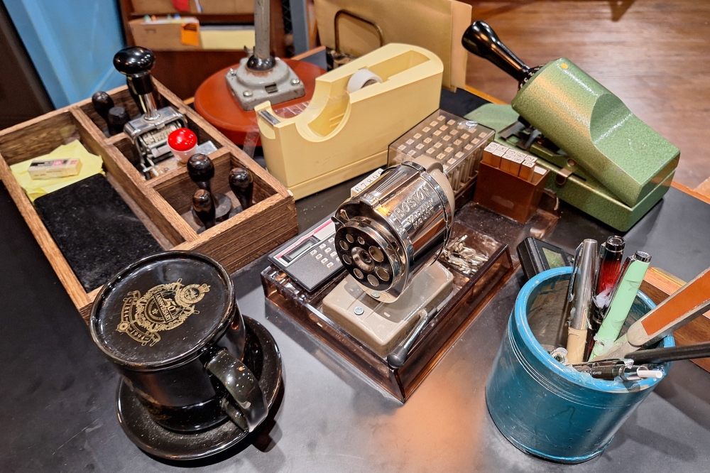 This reimagined desk of a duty officer in the 1970s and 1980s features detailed props, including a Boston Vacuum Mount pencil sharpener, Motorola Advisor pager, a calculator, as well as number and alphabet stamps. — Picture by Ida Lim