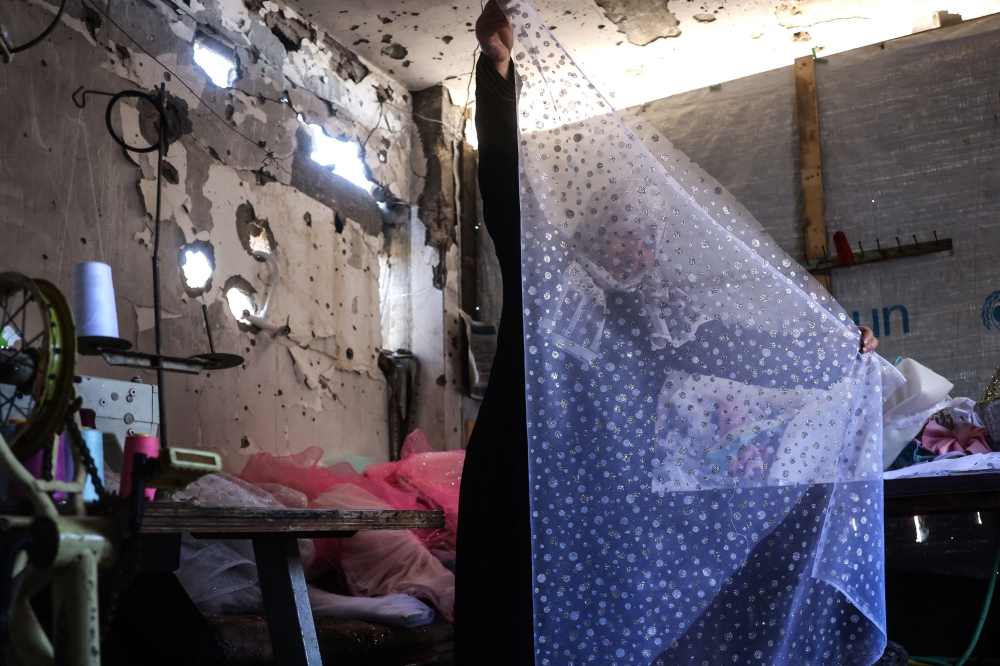 A Palestinian dressmaker folds the cloth for a gown, at a workshop where dresses are created including evening and wedding gowns despite limited resources and old dresses are recycled, in the city of Khan Yunis in the southern Gaza Strip on June 13, 2026. — AFP pic