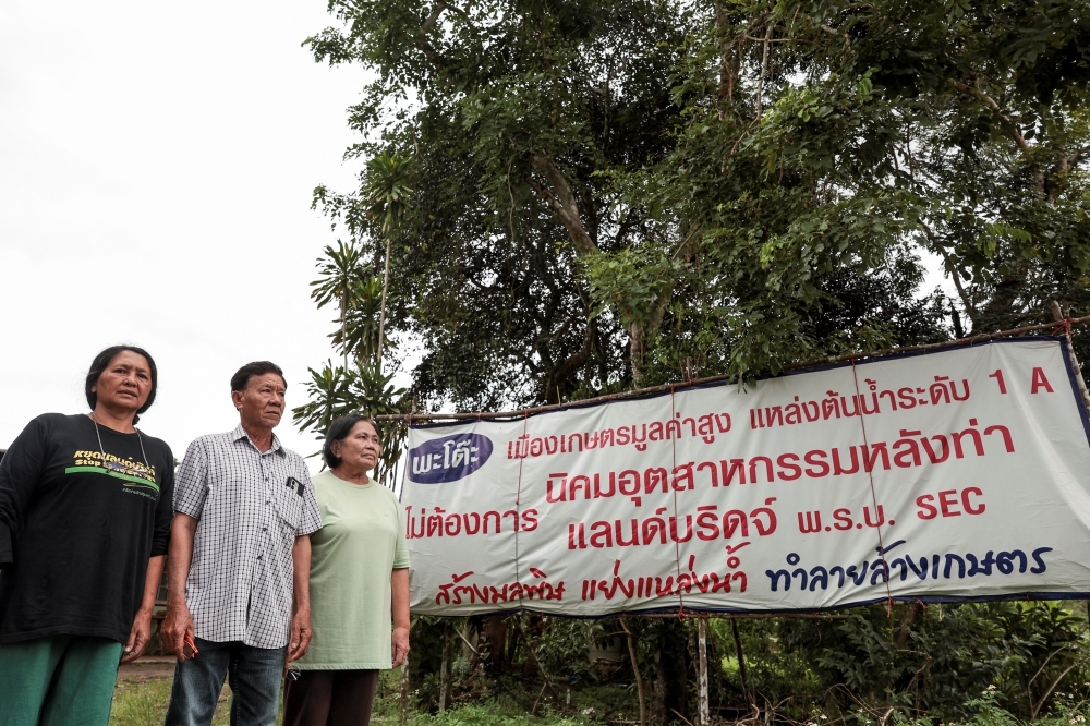 Chalermusa Seekhiao, 56, Sukhon Limratchadawong, 69, and Benchawan Tubtimtong, 66, local farmers in Phato district, pose for a picture near a banner opposing Thailand's proposed Southern Land Bridge project over concerns about its impact on local agriculture and water resources, in Chumphon province May 18, 2026. — Reuters pic  