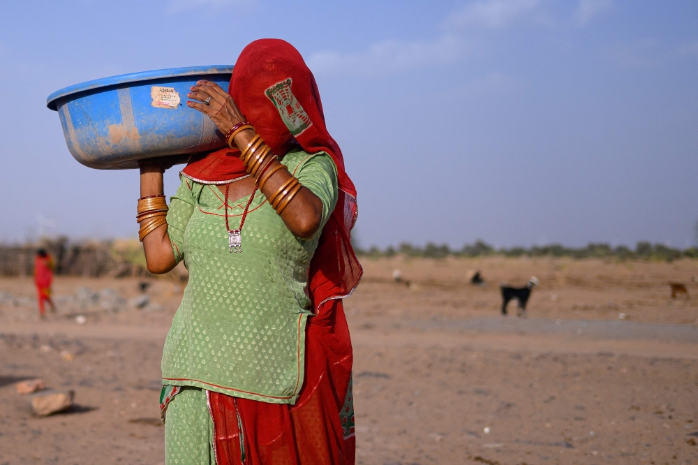 Seema Kawar carries a plastic pan after feeding cattle outside her house in Sanwata village on the outskirts of Rajasthan’s Jaisalmer city when temperatures surpass 40°C. — AFP pic