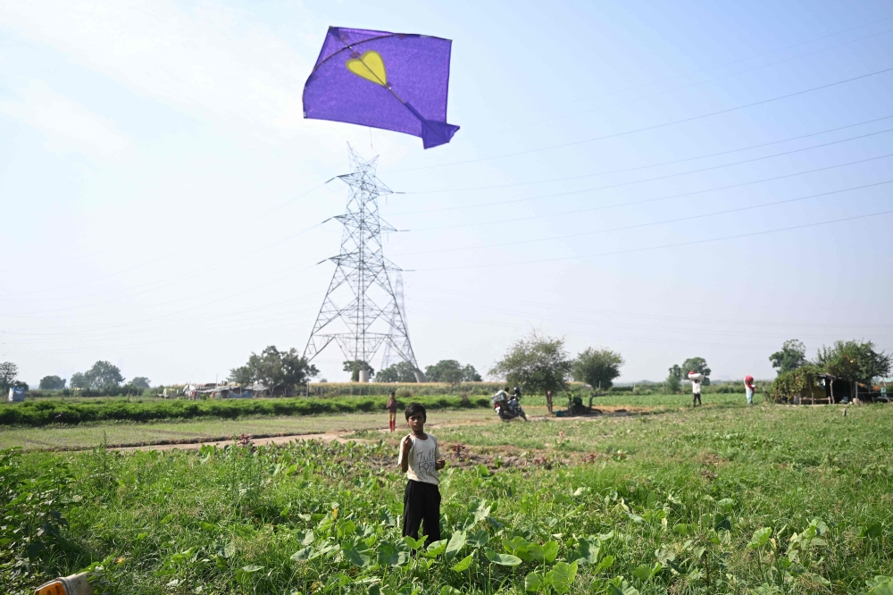 Farmer Bhole Shankar’s son,Tejpal flies a kite outside their home underneath power lines on the Yamuna river floodplains in New Delhi, but their hut is not connected to the electricity grid even as temperatures cross 40°C. — AFP pic